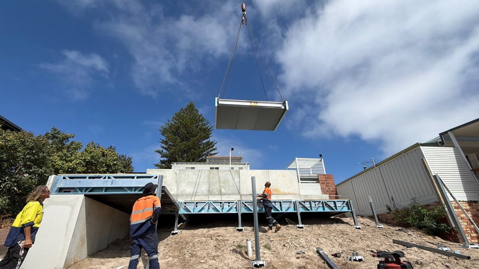 Crane lifting a prefabricated floor cassette onto a steel sub-floor on a sloping Perth block