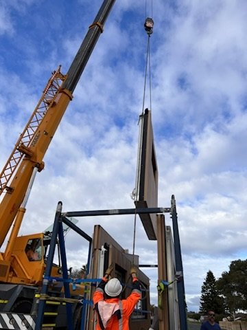 Crane lifting a timber-clad wall panel into place on the Padbury build