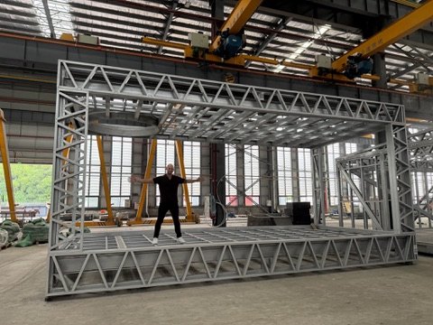 Alex Dennis standing inside a steel module frame in a factory